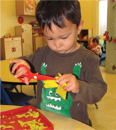 Young boy using scissors at a classroom crafts table