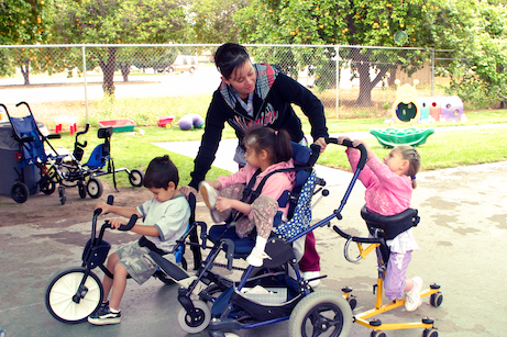 Care giver in a school yard with three children using assistive devices